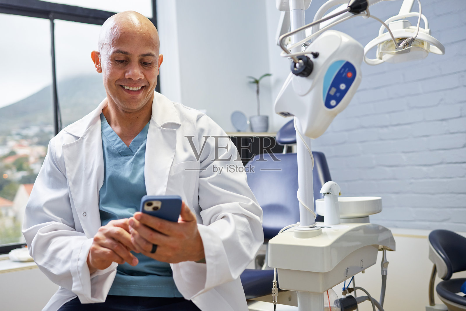 微笑的牙医在现代牙科办公室休息时使用智能手机照片摄影图片