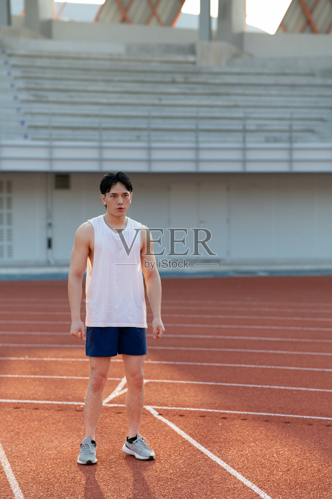 一位穿着白色背心的亚洲男子站着，向前看，正在跑步后休息。照片摄影图片