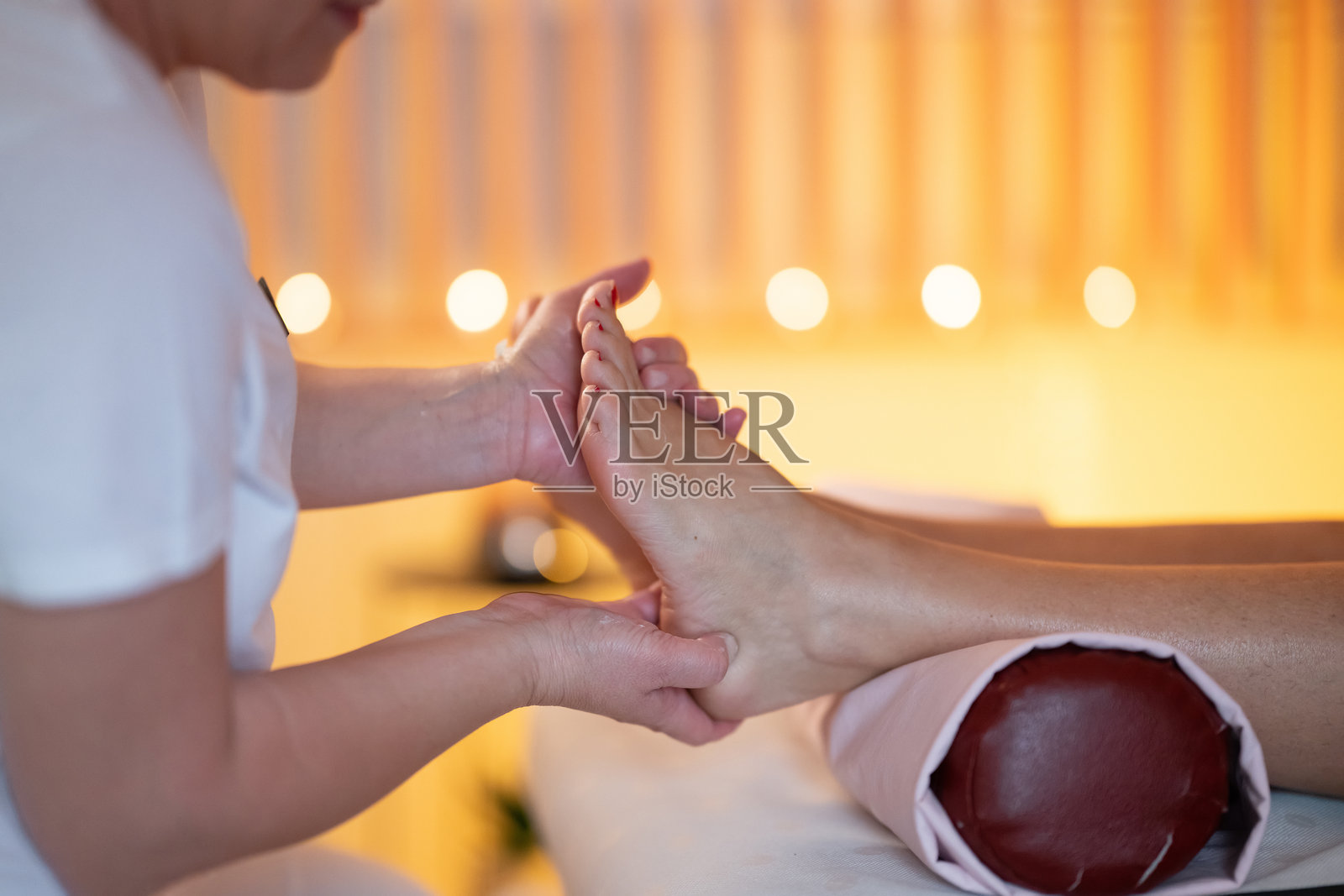 放松水疗环境中的足部按摩疗法。一位穿着白色制服的专业按摩师在宁静舒适的水疗环境中为客户提供舒缓的足部按摩。照片摄影图片