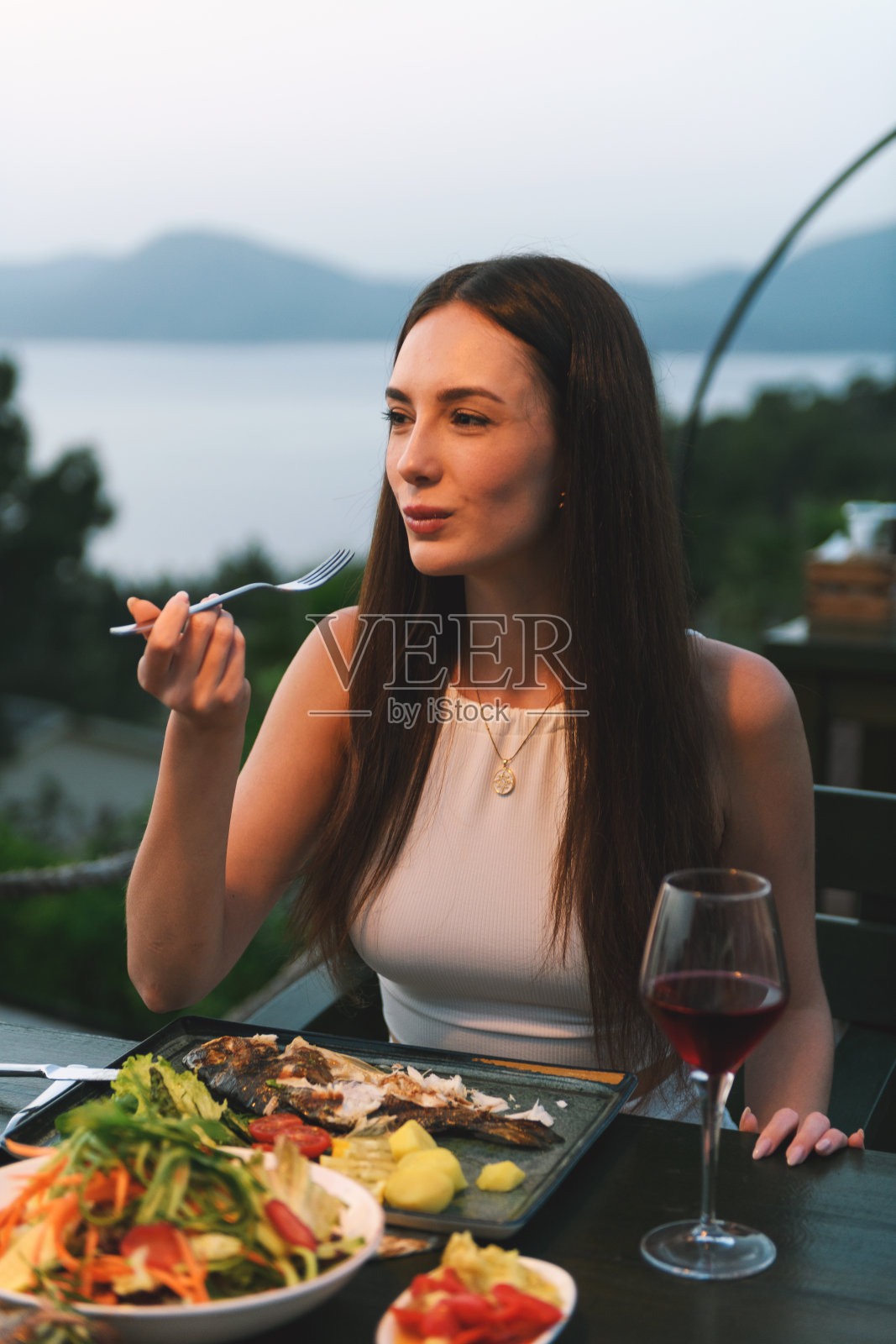 一位20多岁的棕发女性在豪华酒店餐厅优雅的氛围中享受她的晚餐和美酒。照片摄影图片