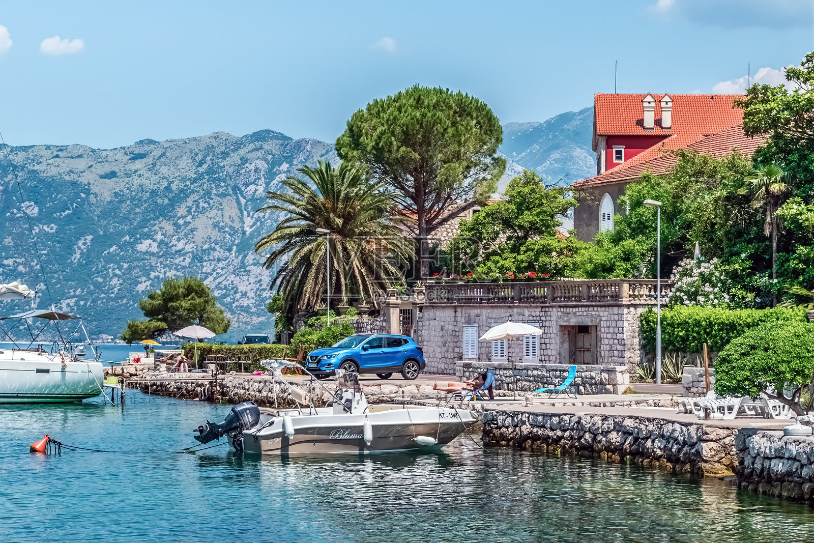 科托尔海滨的放松场景，停靠着船只，岸边的房屋旁有一个人在日光浴。照片摄影图片