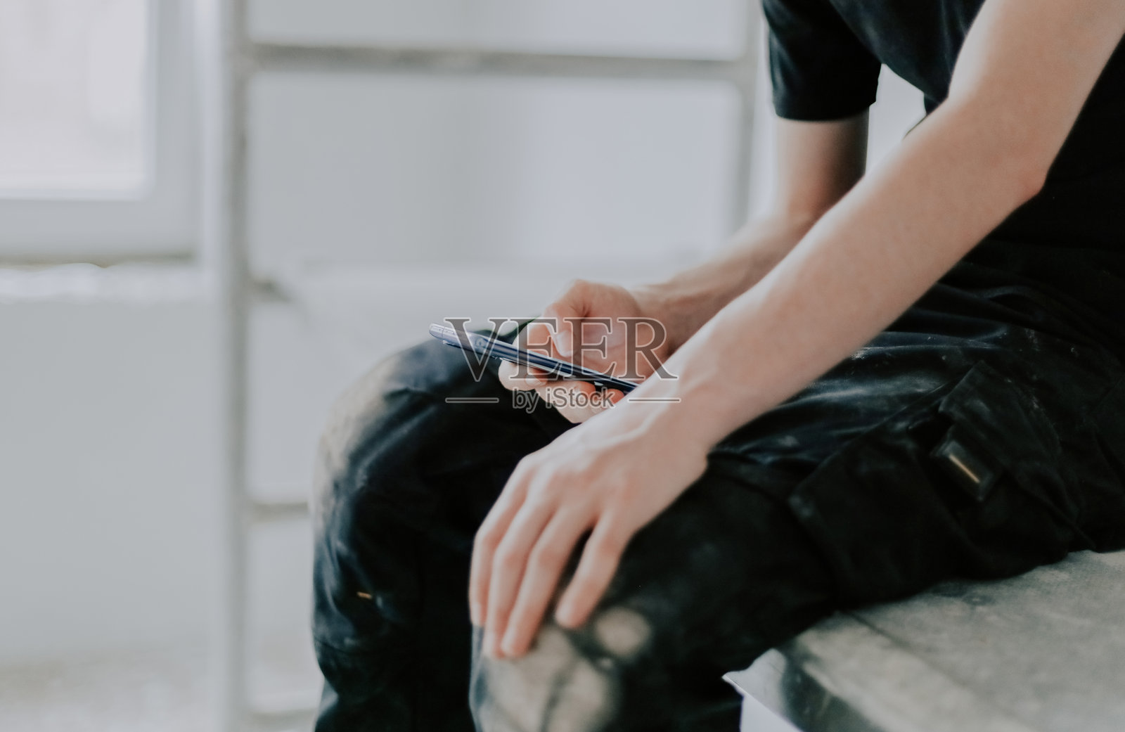 一名年轻工人坐在脚手架上，手中拿着智能手机。照片摄影图片