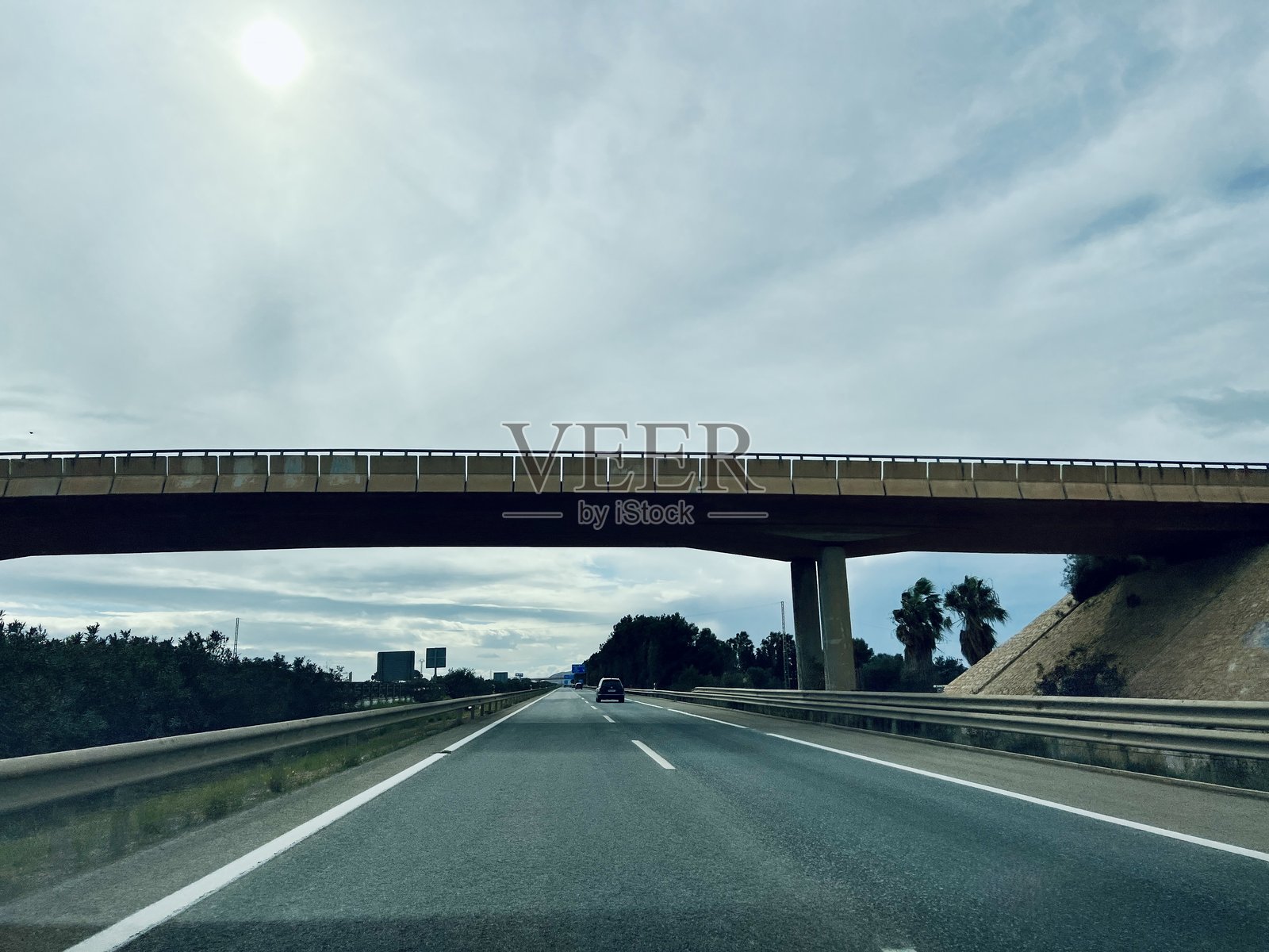 西班牙圣哈维尔 - 2025年3月9日：风景如画的高速公路在大型高架桥下，路边种满了棕榈树，天空多云。照片摄影图片