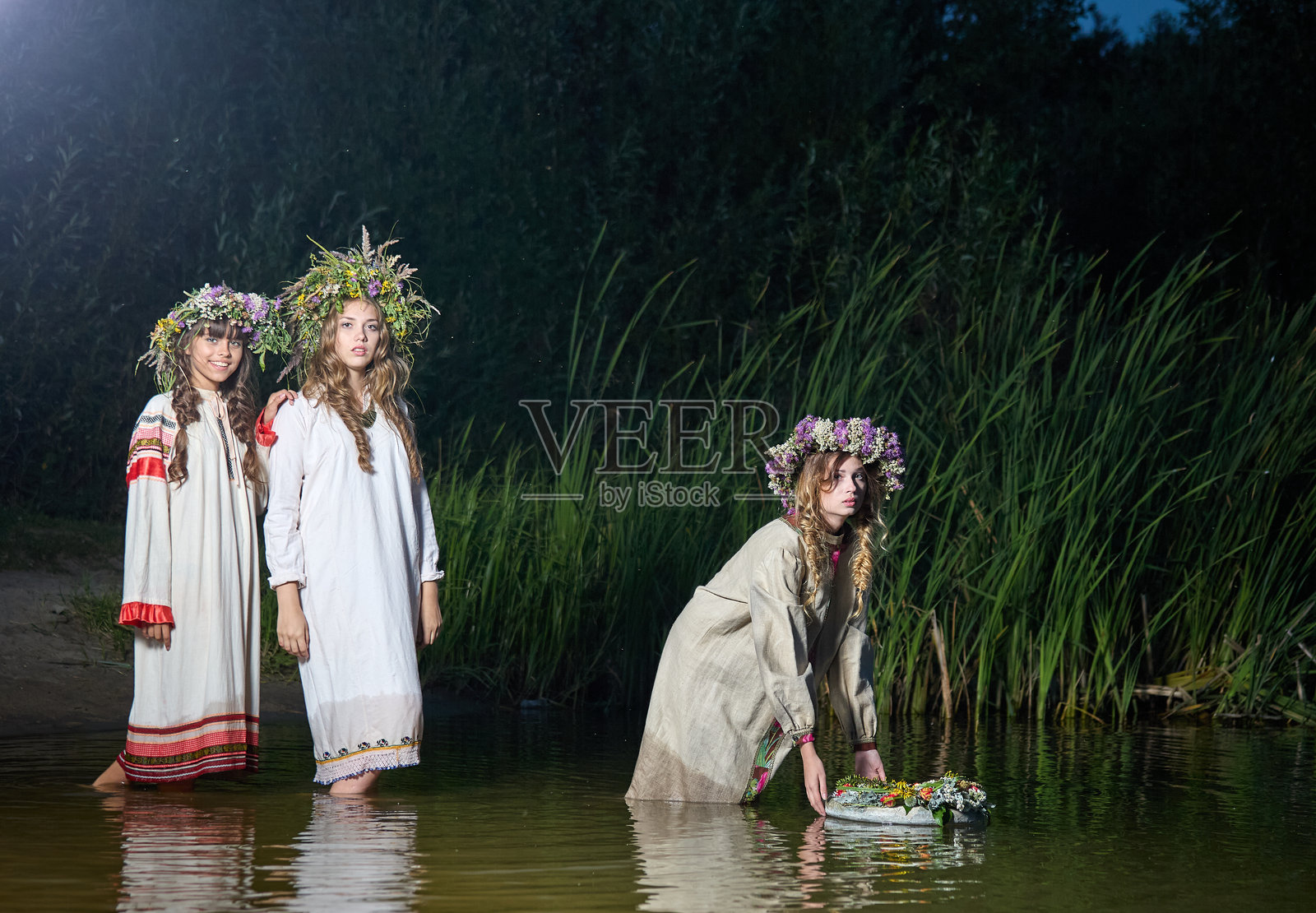 古老的斯拉夫婚姻占卜习俗，在仲夏之夜，三位身着民族服饰的美丽年轻女性将花环放入河中。照片摄影图片