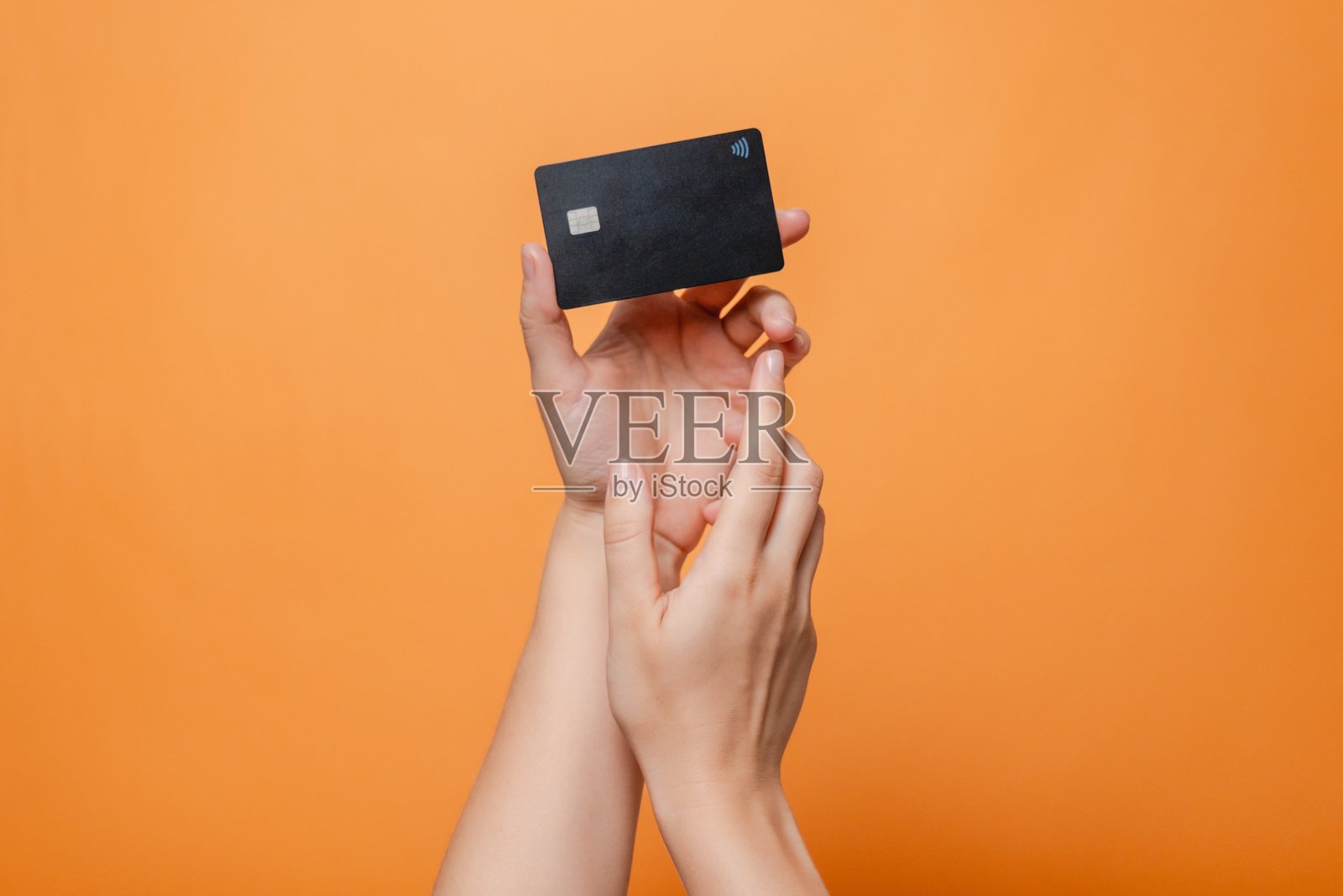 优雅的手握着空白信用卡，适用于在线服务的模拟图，背景为橙色。现代银行和购物方式。照片摄影图片