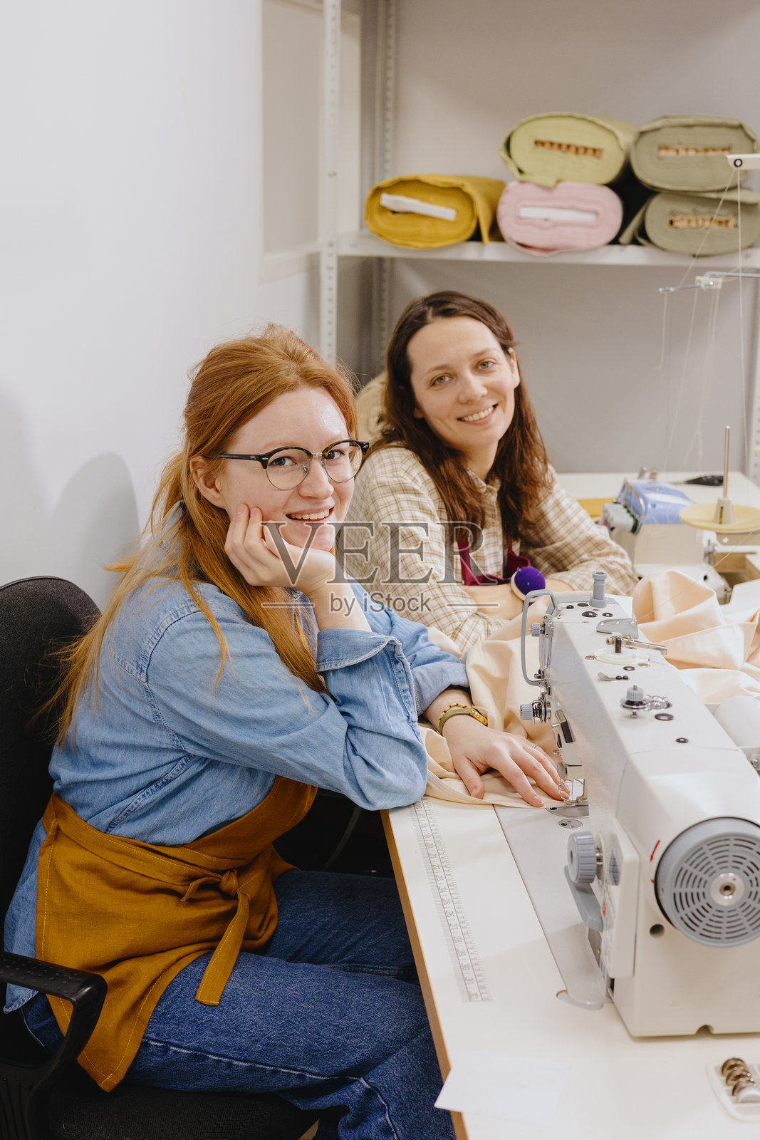 两名女裁缝在工厂的车间里，正在缝纫机旁的桌子上工作。照片摄影图片