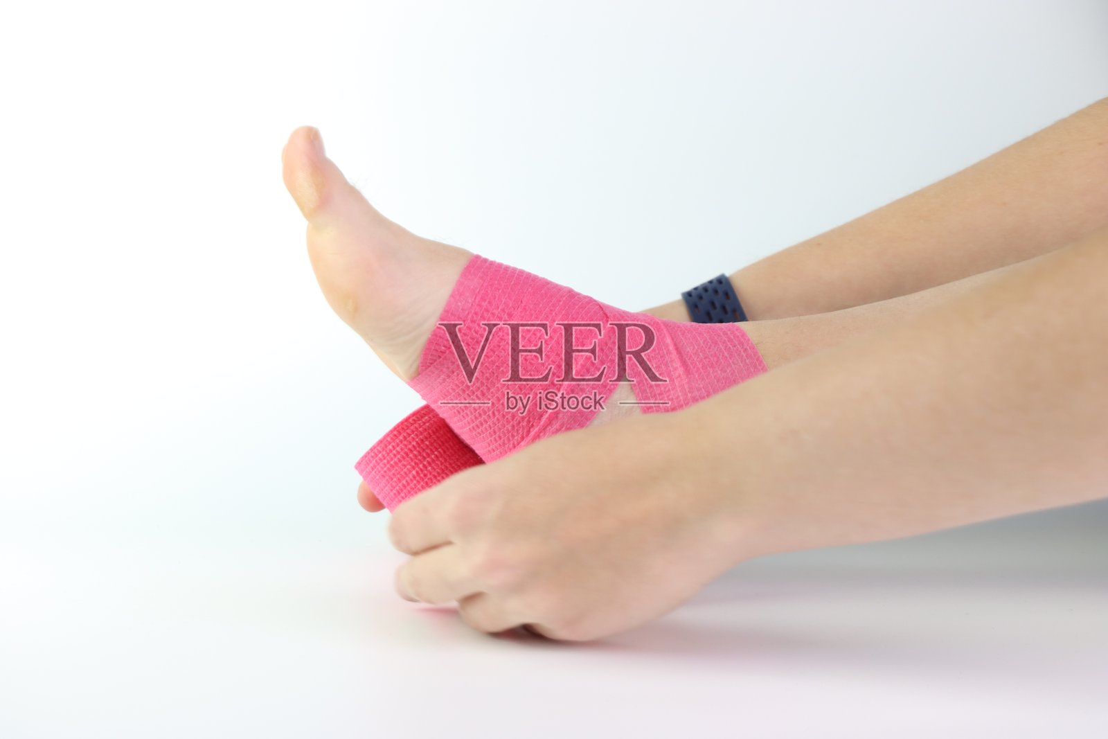 女性脚踝上缠绕着粉色绷带，背景为白色。照片摄影图片