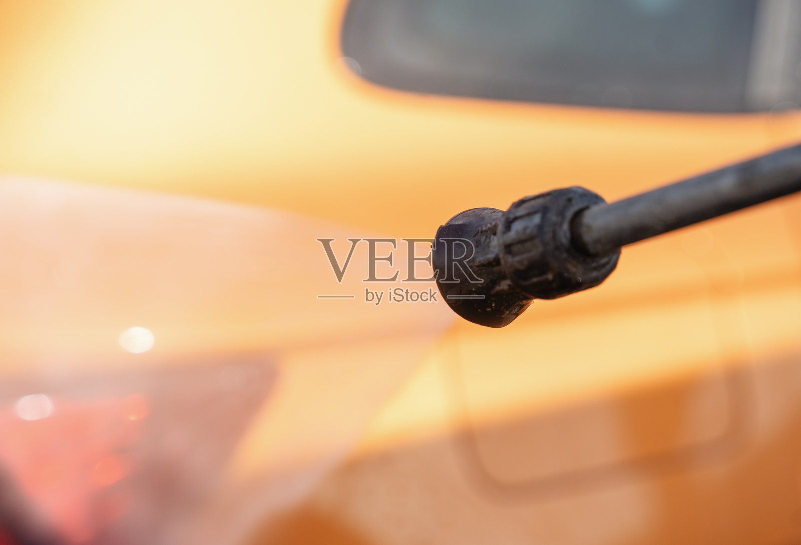 在阳光明媚的周末，驾驶员在一个户外场所用高压清洗机清洗一辆橙色汽车，水花四溅。照片摄影图片