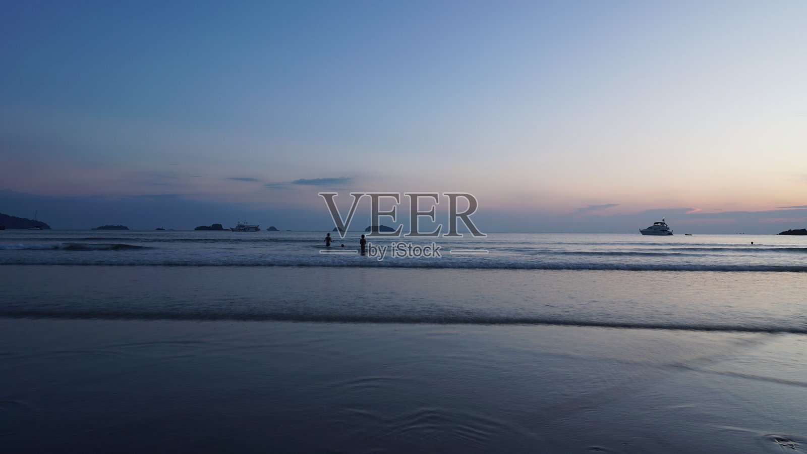 游客们在黄昏时分享受热带海洋，远处有船只。照片摄影图片