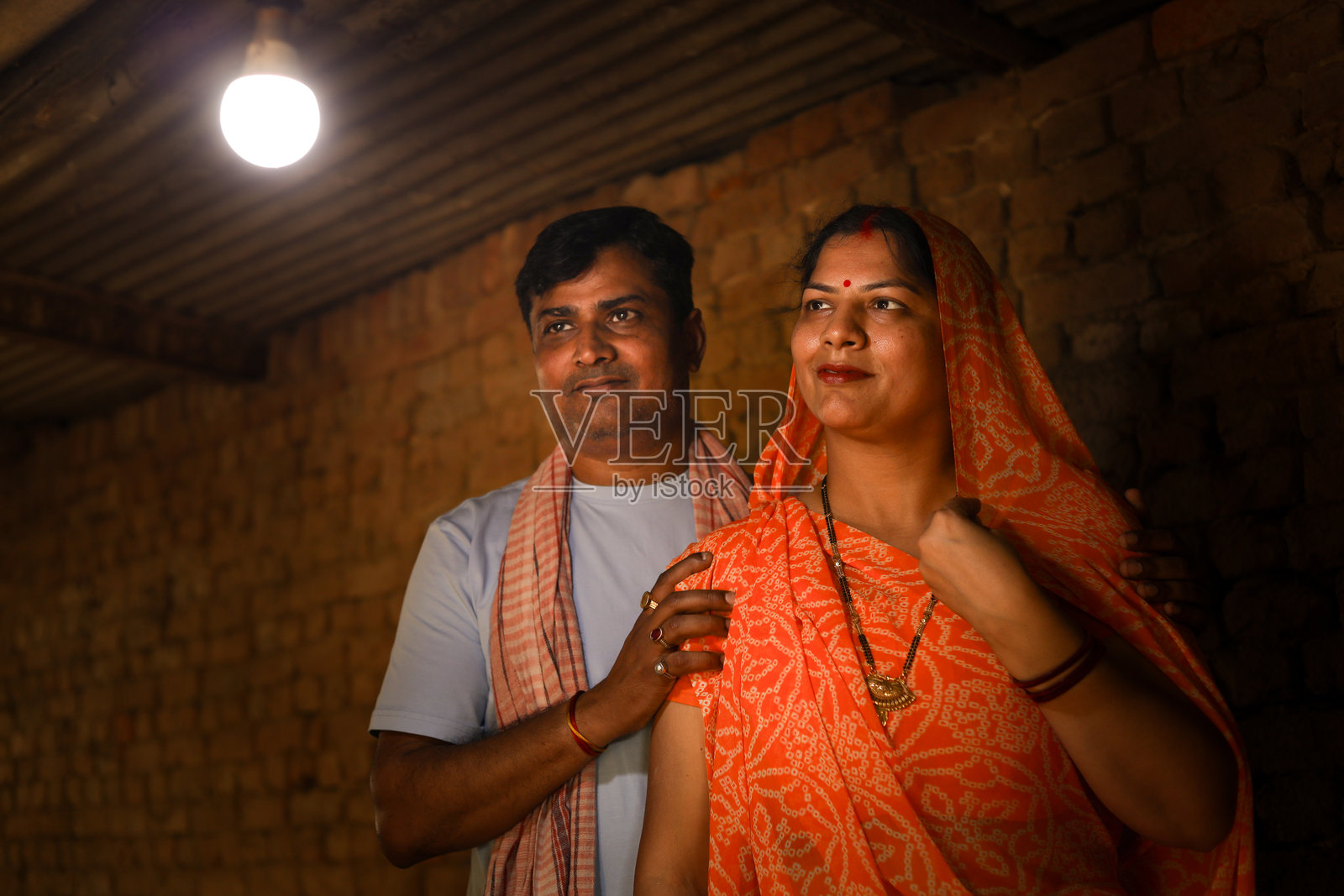 乡村印度夫妇高兴地看到电力到达他们的家。村民夫妻看着电灯泡。照片摄影图片