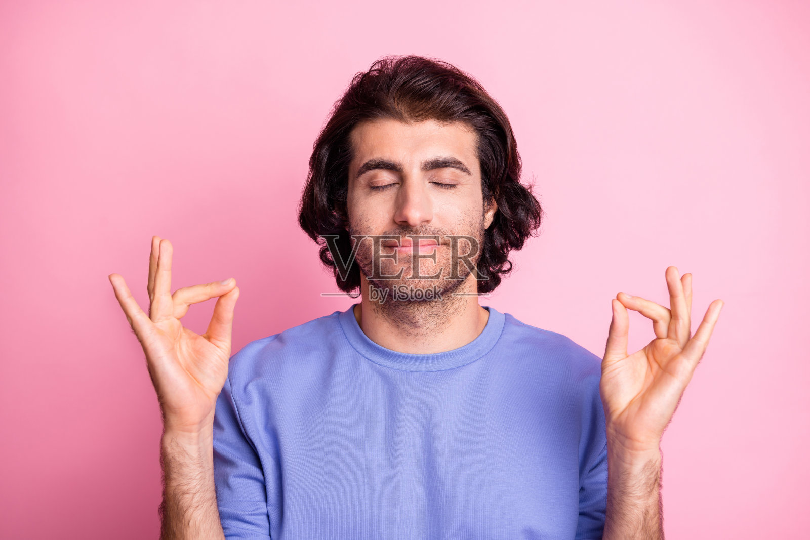 穿着紫色毛衣的年轻男子在粉色背景下冥想，做出OM手势，显得平静放松。照片摄影图片