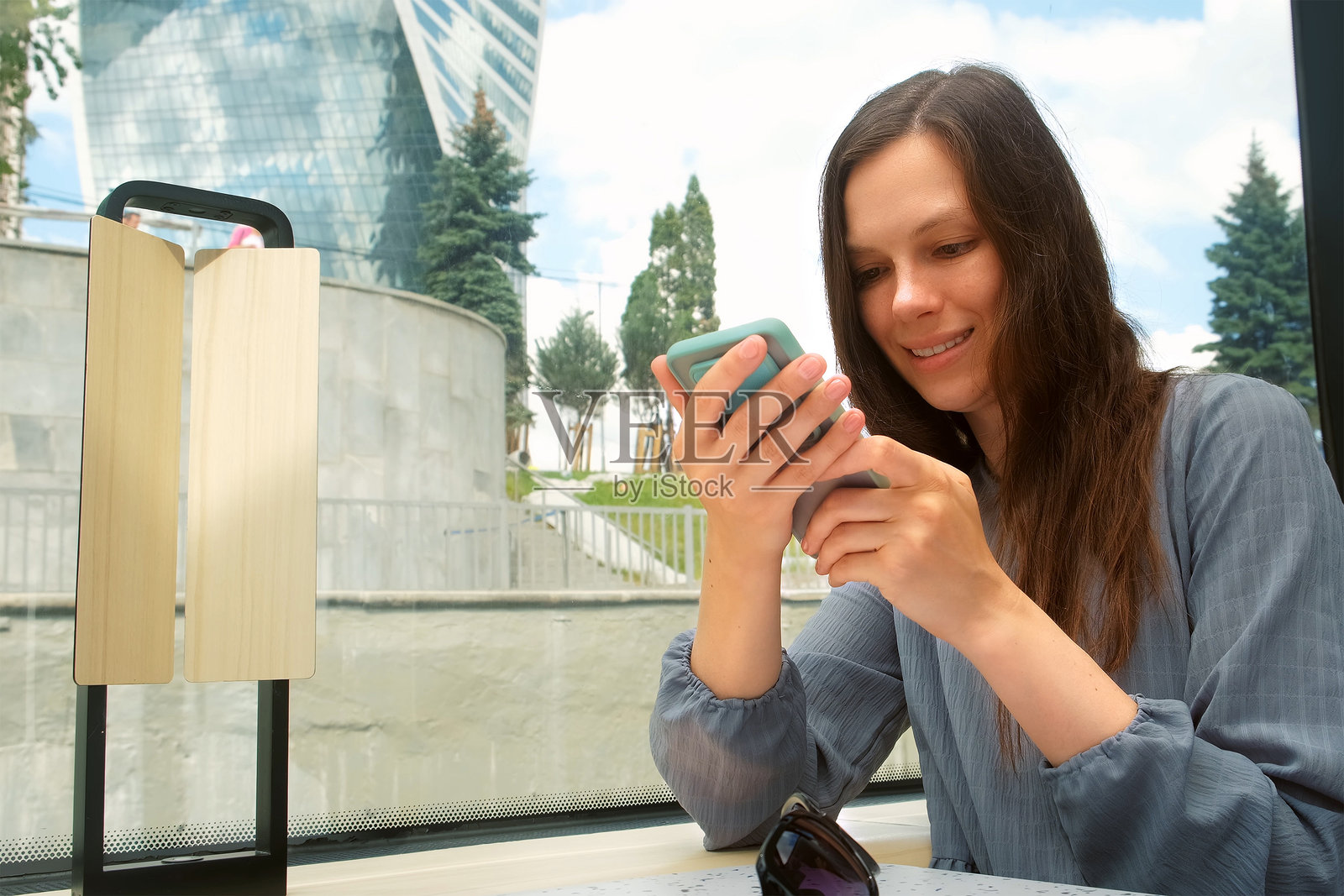 微笑的女性坐在城市的河流电车上，盯着智能手机。照片摄影图片