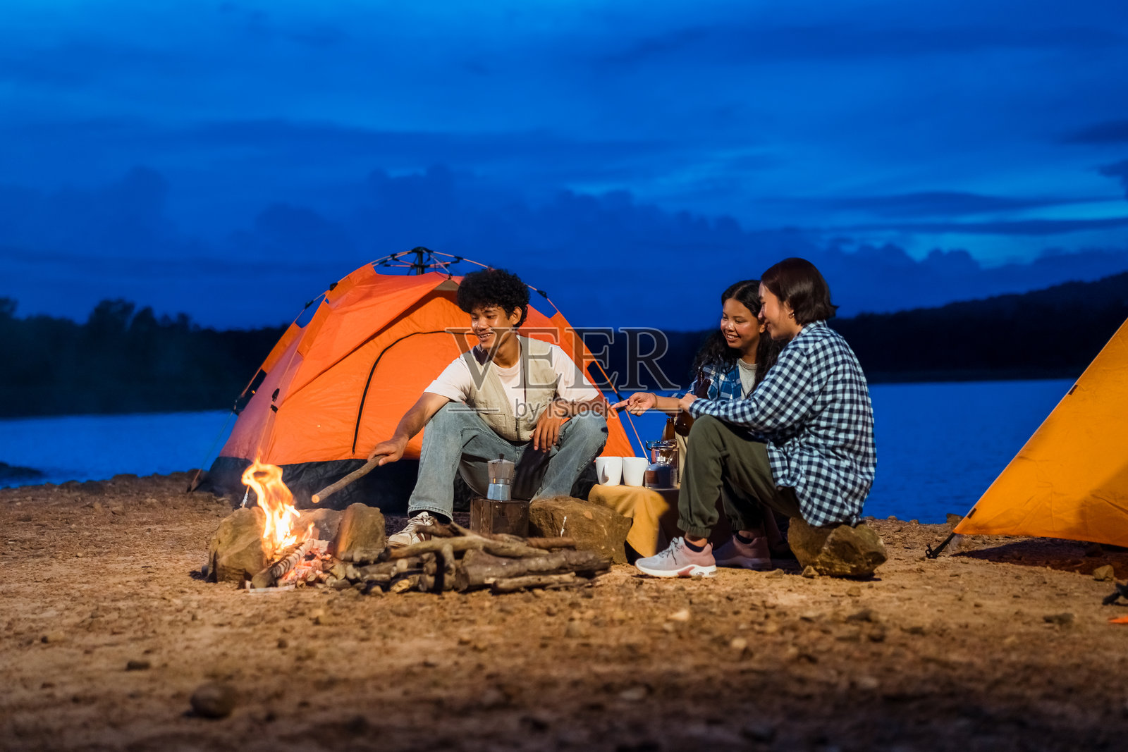 三个人坐在帐篷里的篝火旁。朋友们享受户外露营，庆祝友谊、联系和团结的时刻。照片摄影图片