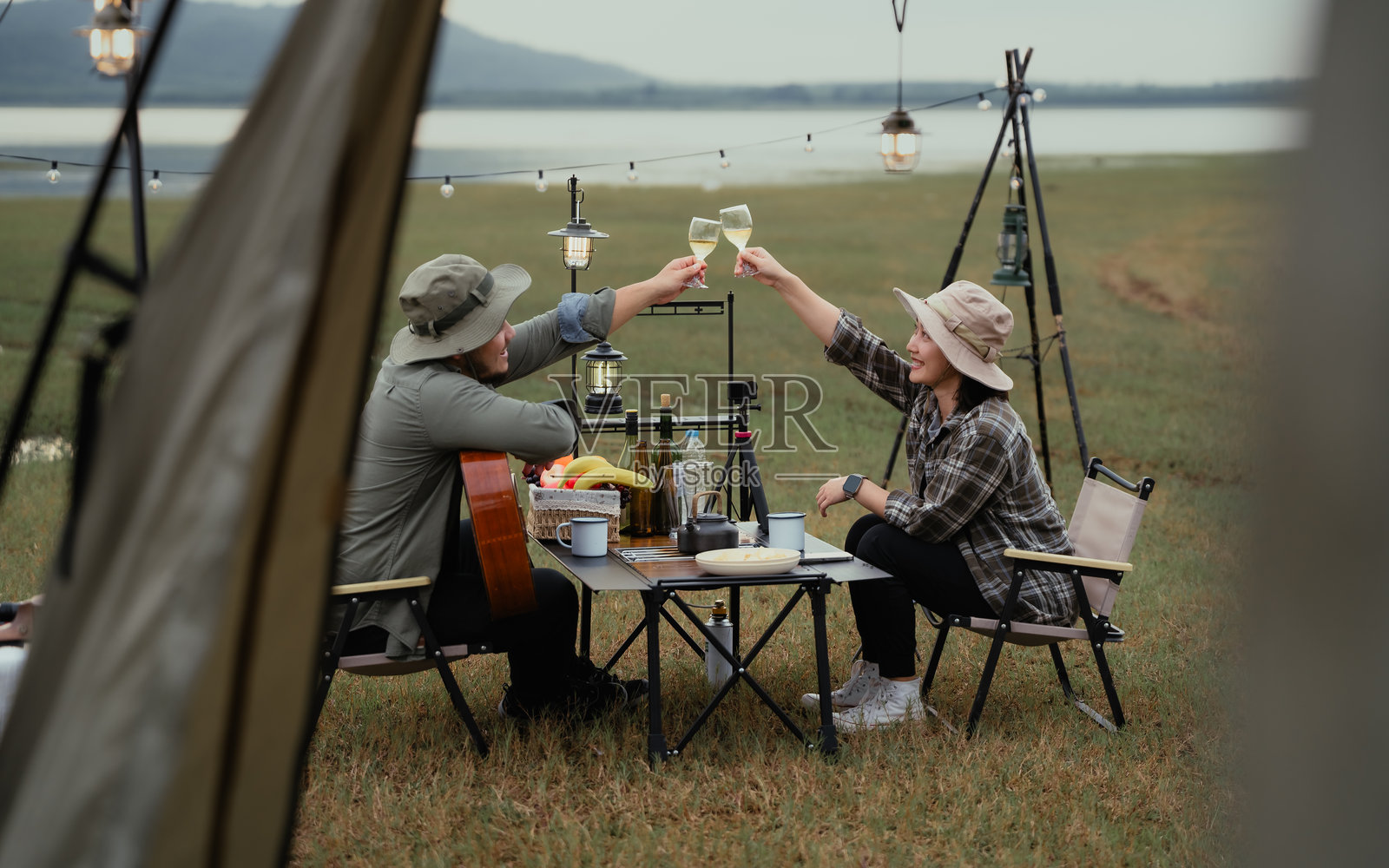 一男一女坐在桌子旁，桌上有酒杯和一瓶酒。他们互相举杯祝酒。露营户外生活方式概念。照片摄影图片