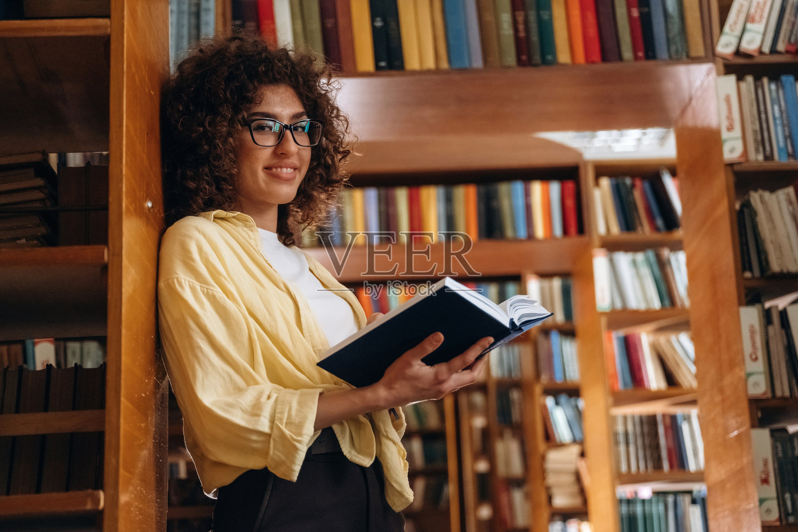 靠在书架上。美丽的女人在图书馆里。照片摄影图片