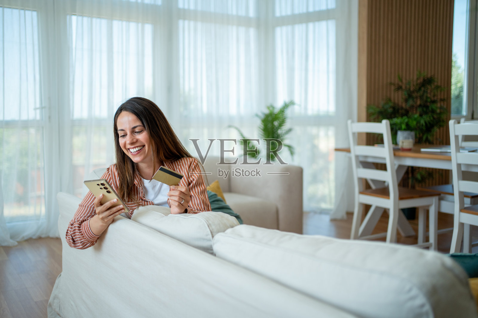 年轻女性在家中使用智能手机和信用卡进行在线购物照片摄影图片