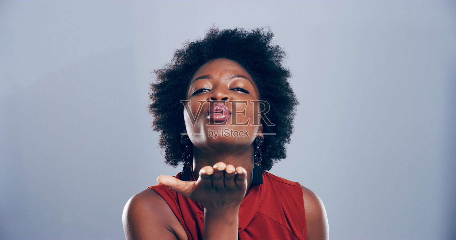 撅嘴的女性在工作室中吹吻，和浪漫手势，适合情人节或其他场合。蓝色背景，黑人的表情展现爱意，快乐的女孩肖像。照片摄影图片