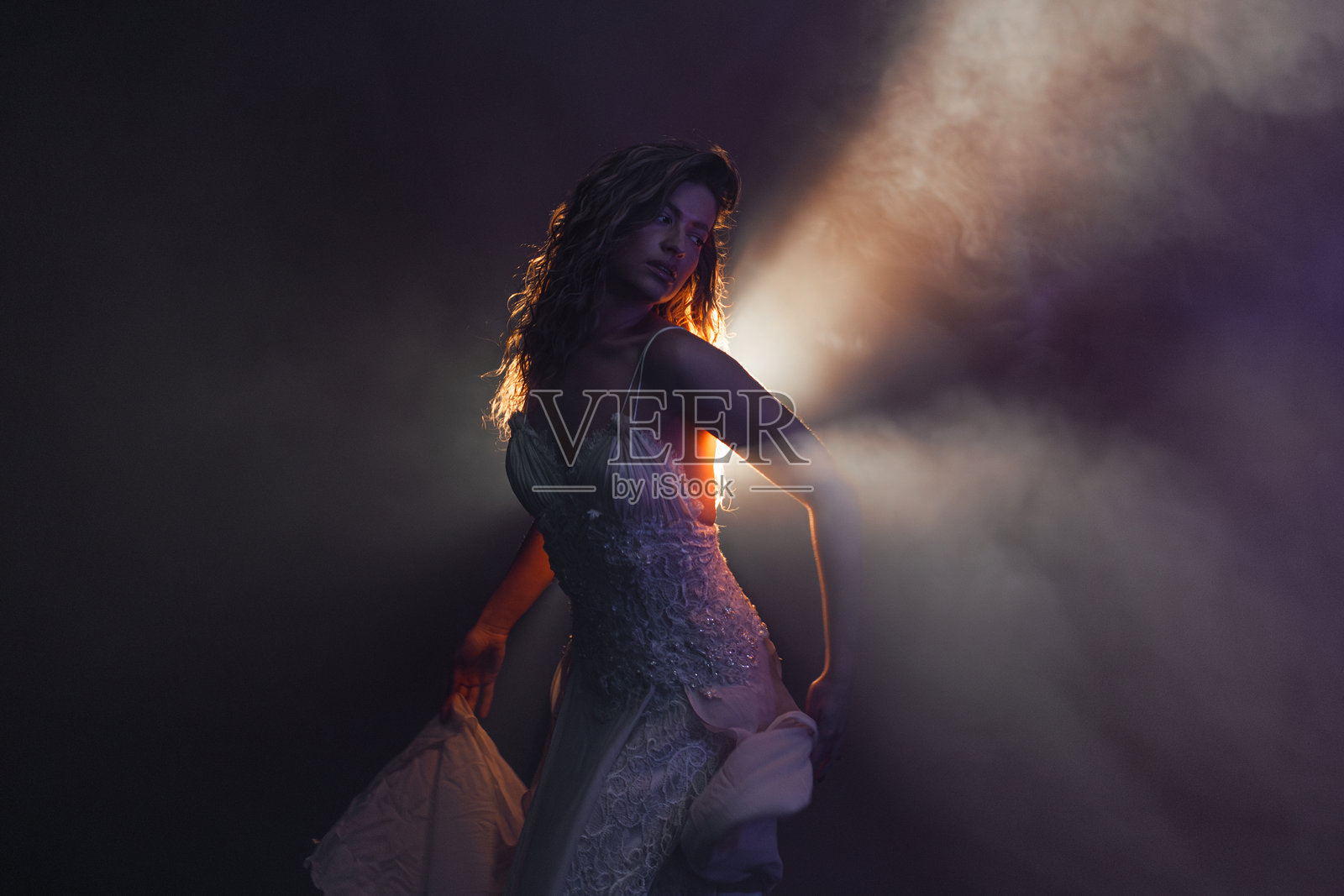 在神秘的背光中，穿着白色裙子的飘渺女子在舞动，营造出电影般的朦胧和戏剧效果。照片摄影图片