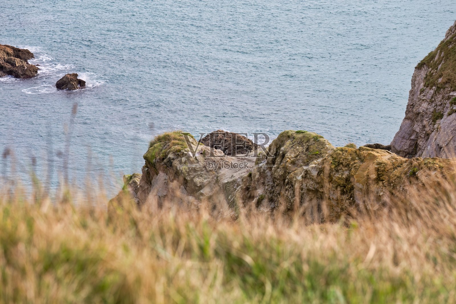 一处草地悬崖俯瞰着平静的水面和岩石突起。照片摄影图片