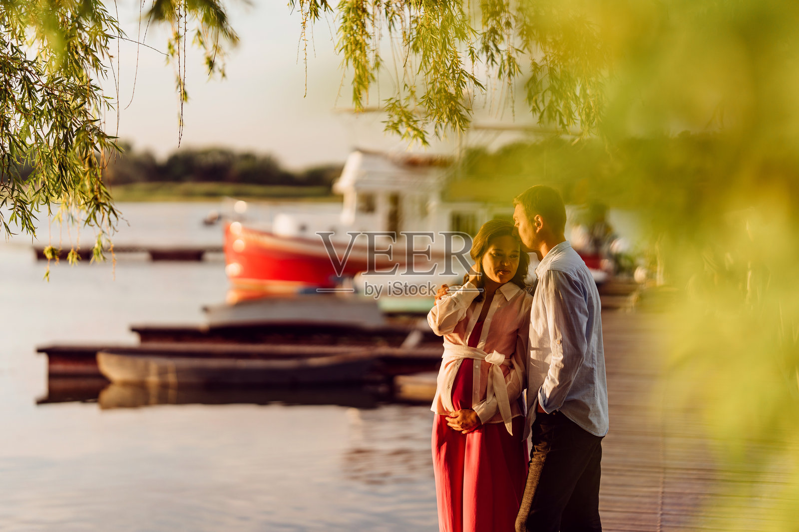 穿着红色裙子的男人和孕妇在码头日落时分。照片摄影图片