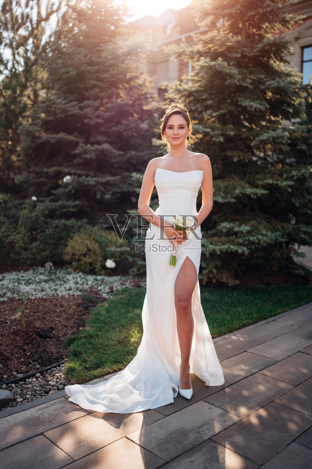 美丽的棕发新娘穿着紧身婚纱，手捧一束马蹄莲。照片摄影图片