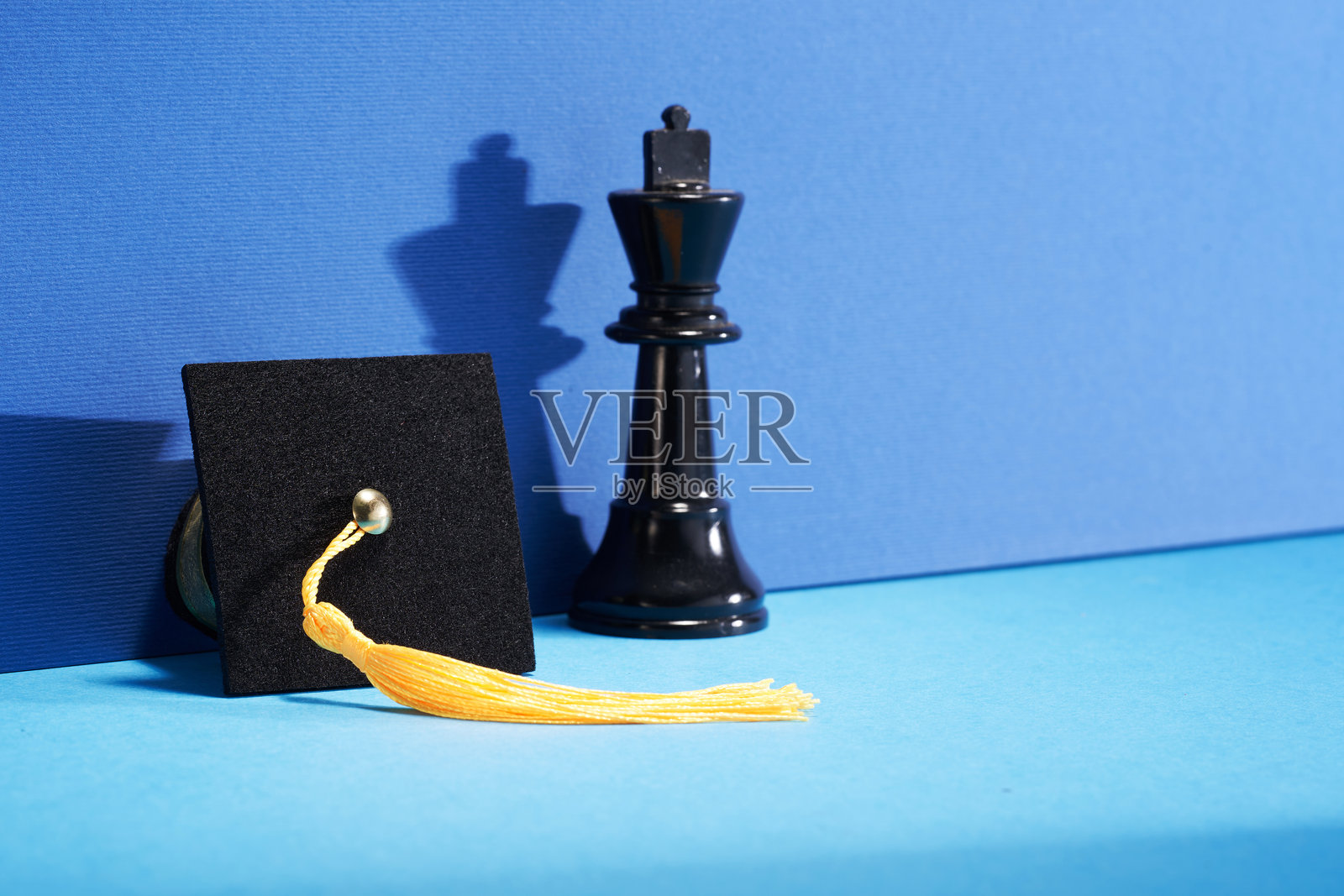 蓝色背景下的国王棋子和小学位帽照片摄影图片