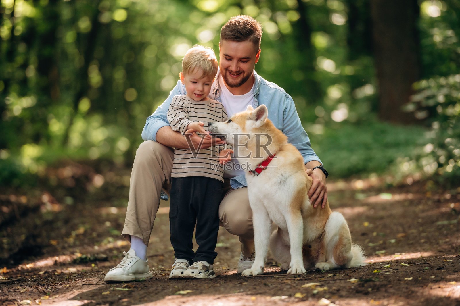 快乐的父亲与儿子和狗在森林里坐着微笑。照片摄影图片