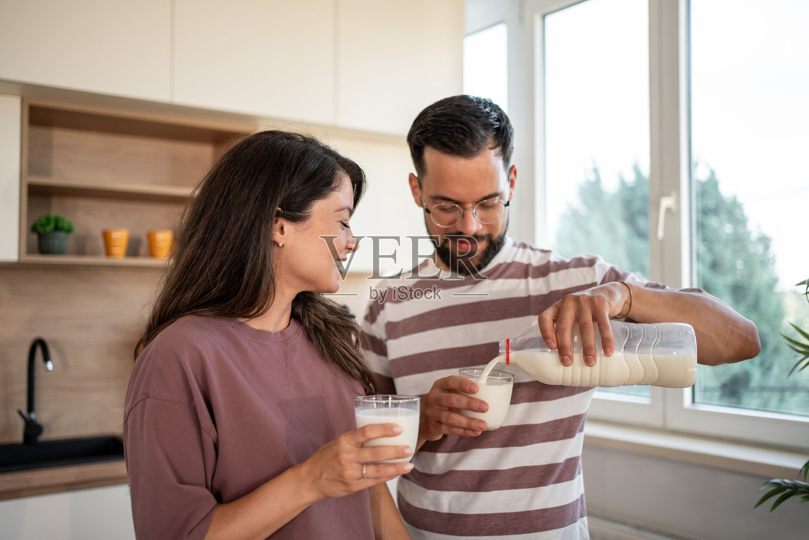 年轻情侣在现代厨房里往杯子里倒牛奶照片摄影图片