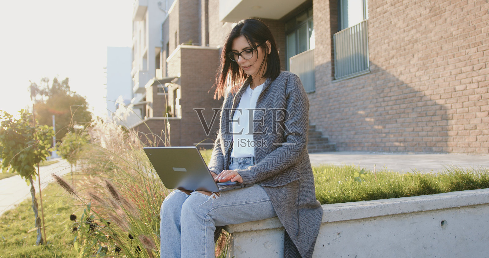 迷人的白人忙碌女性在街上休息时坐着，使用笔记本电脑工作和输入文本。户外环境。照片摄影图片