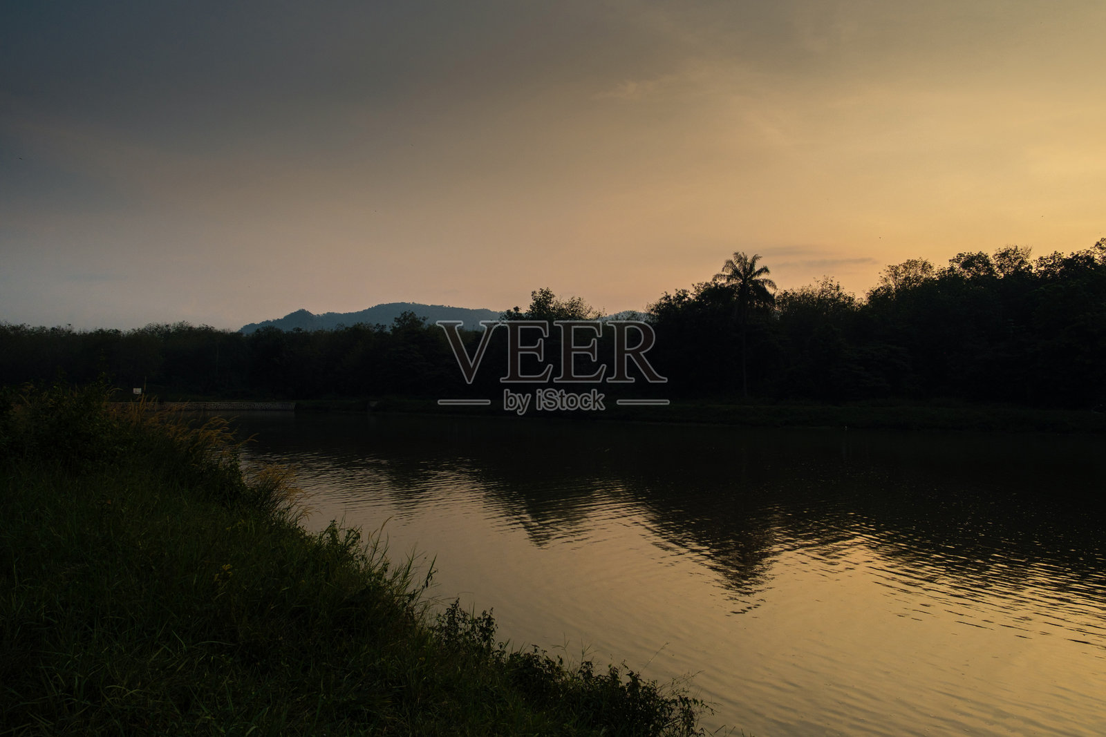 宁静的日落映照在平静的河边，树木的剪影倒映在水面上照片摄影图片