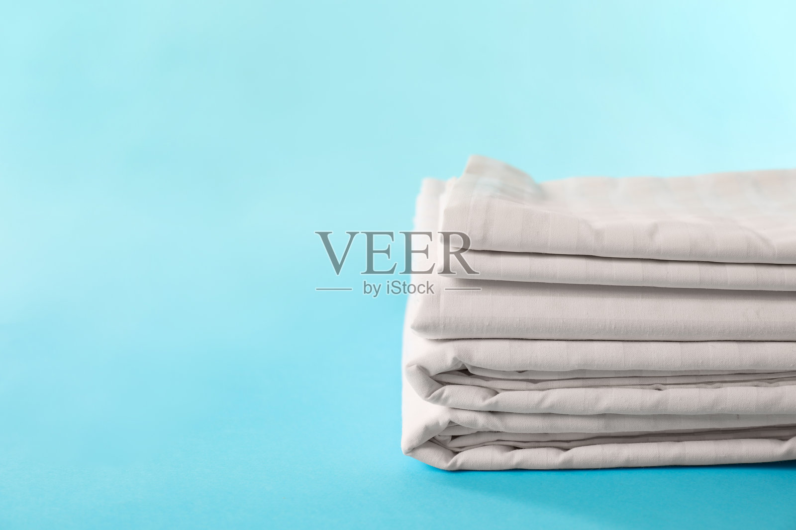 叠放整洁的床单在浅蓝色背景上，留有文字空间照片摄影图片