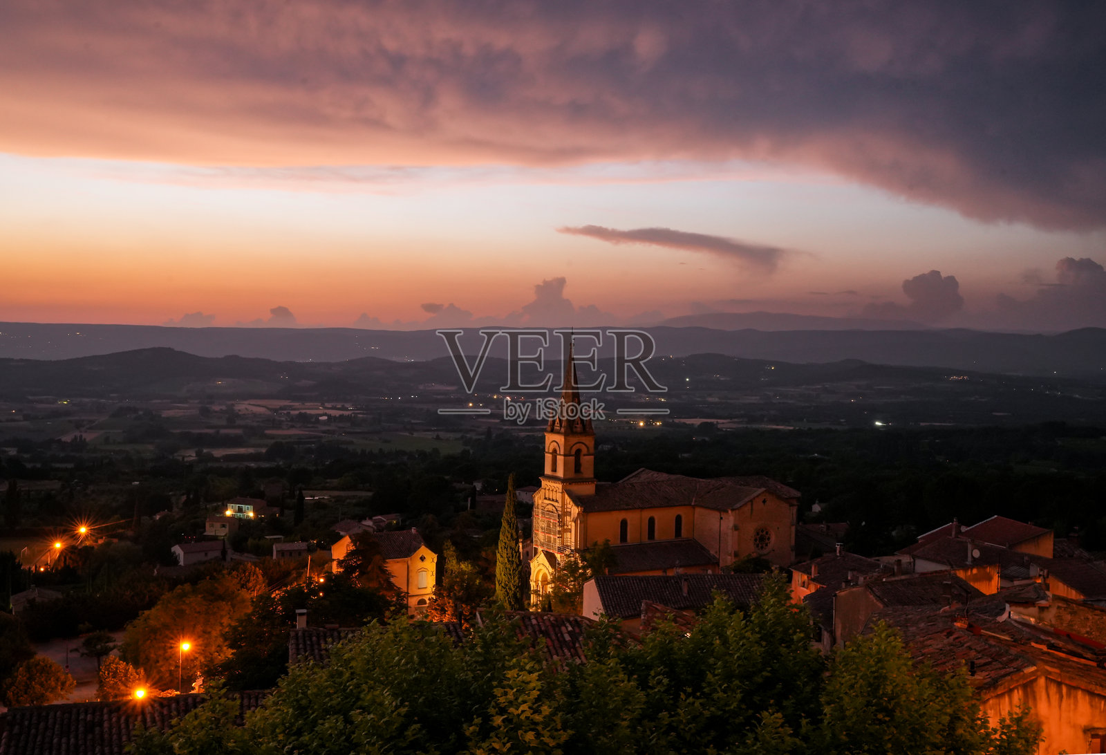 法国普罗旺斯吕贝龙的博尼厄村，傍晚时分，街灯点亮。村庄俯瞰沃克吕兹山脉和红云映衬的落日天空。照片摄影图片