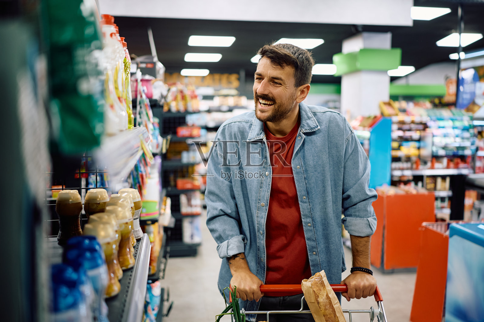 快乐的男人在超市里推着购物车购物。照片摄影图片