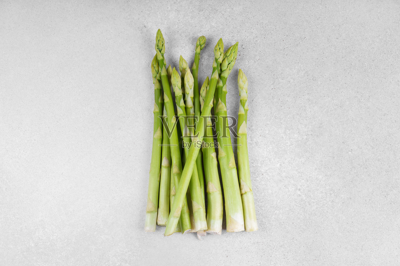 一堆新鲜生的绿色芦笋或雀草茎，放在浅色纹理背景上照片摄影图片