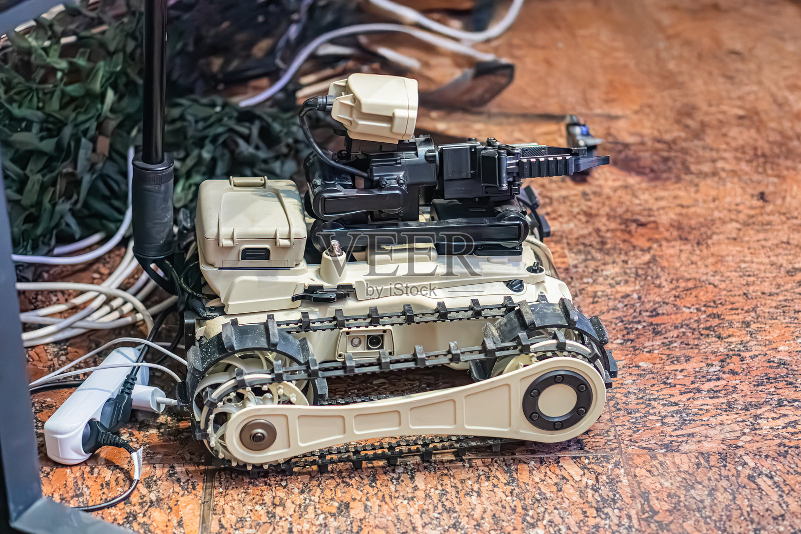 室内技术环境中，一辆米色的机器人坦克特写，可能用于排雷。坦克顶部装有摄像头或传感器系统及其他电子设备。照片摄影图片