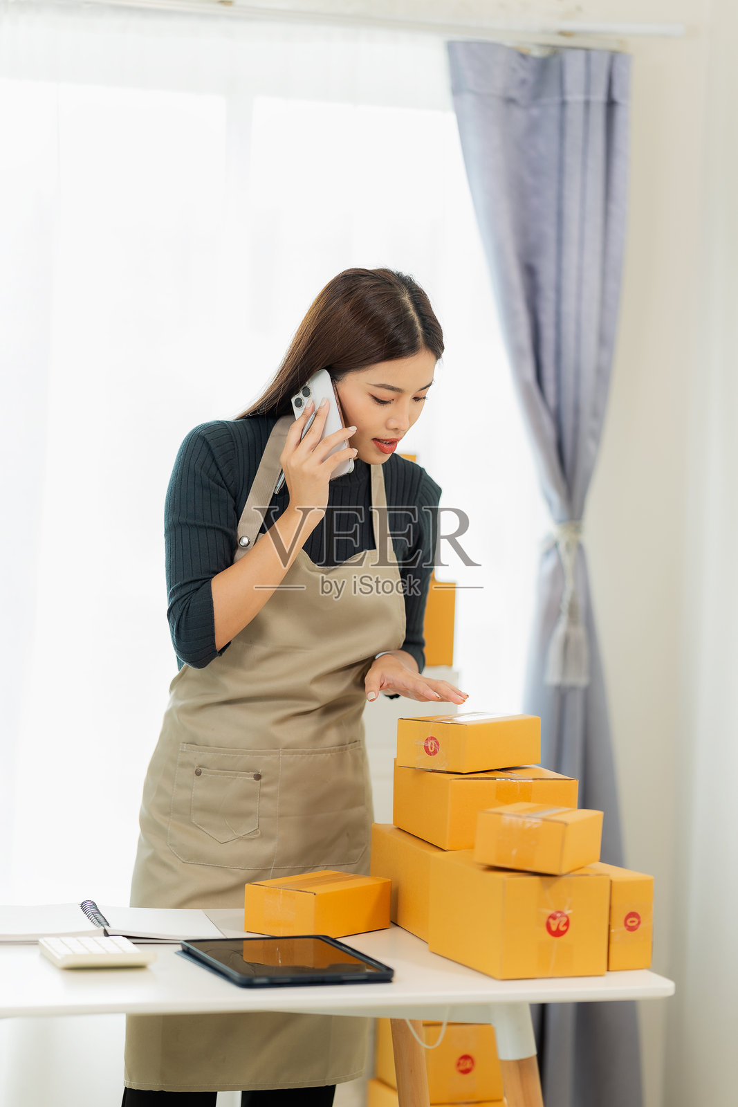 年轻的亚洲女孩是一名自由职业者，在家中经营自己的生意。她使用笔记本电脑，开始了自己的中小企业，涉及在线销售、市场营销、包装和配送，电子商务概念。照片摄影图片