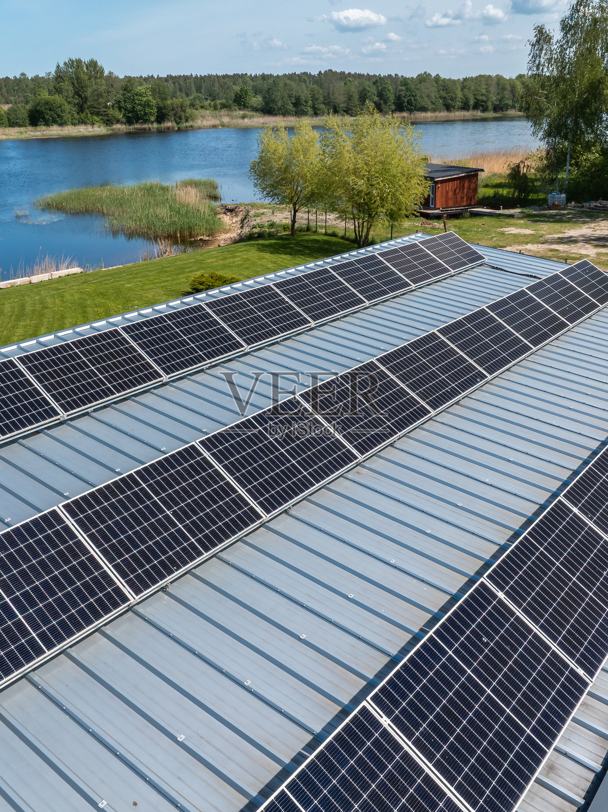 靠近水域和植被的金属屋顶与太阳能电池板照片摄影图片