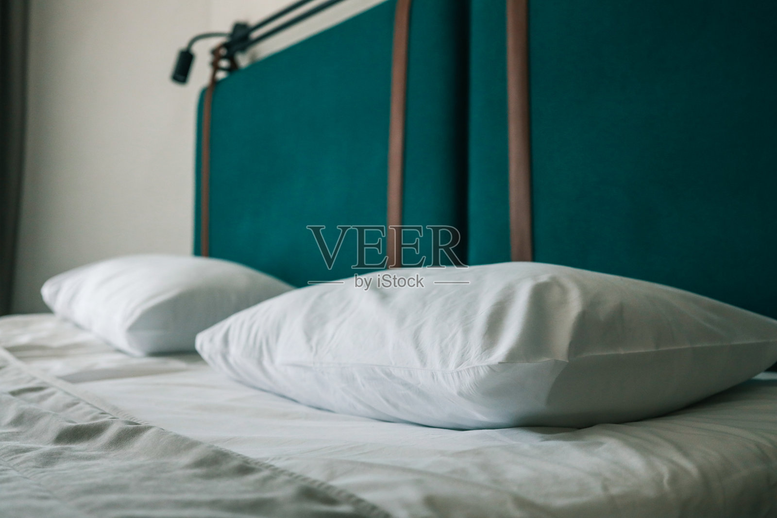 现代酒店床上整齐摆放的洁白枕头特写，搭配青绿色的软垫床头和皮革带，传达出舒适、干净和精品住宿风格。照片摄影图片