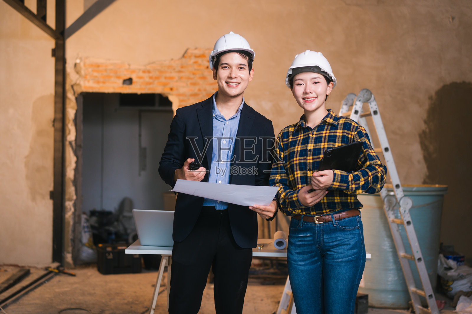 亚洲男女工程师正在检查建筑蓝图，并审查钢材和石灰石的材料成本，为建筑项目准备竞争性投标提案，与项目团队合作。照片摄影图片