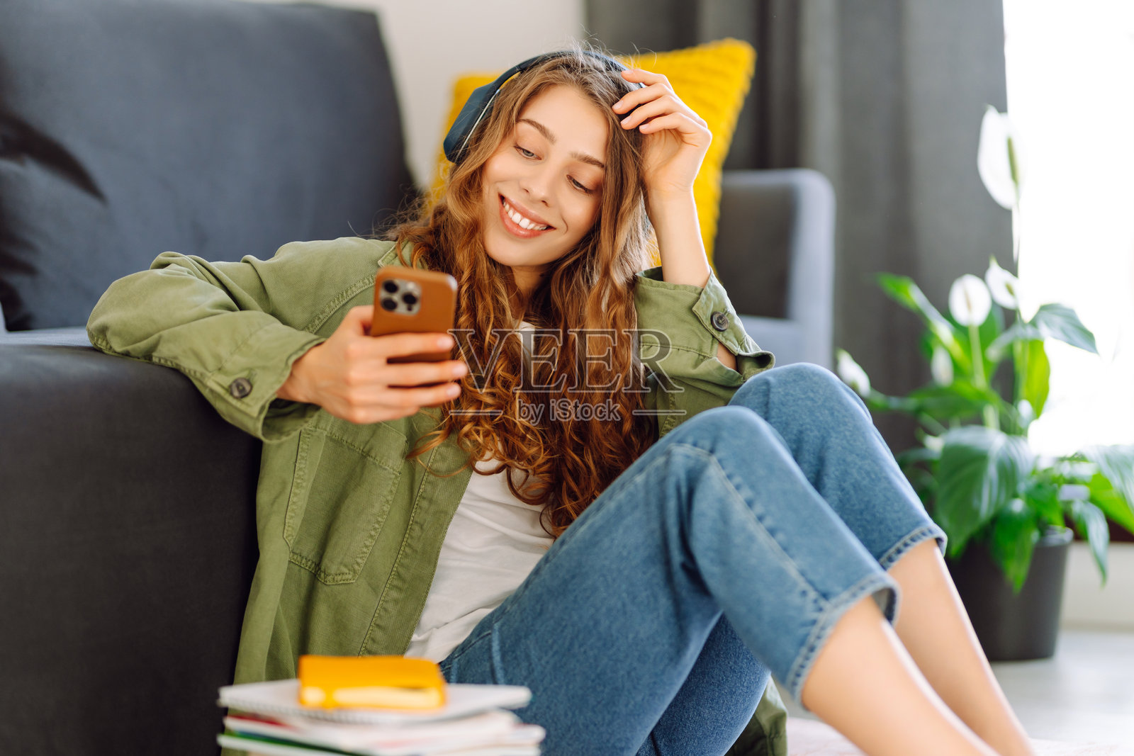 可爱的女人在舒适的客厅里享受听音乐和放松，手中拿着手机。照片摄影图片