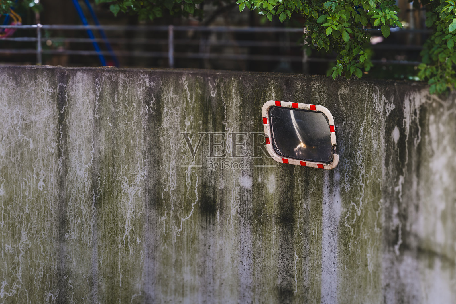 镜子映照出一个安静的公园角落，墙壁斑驳，绿意盎然，沐浴在傍晚的阳光中。照片摄影图片