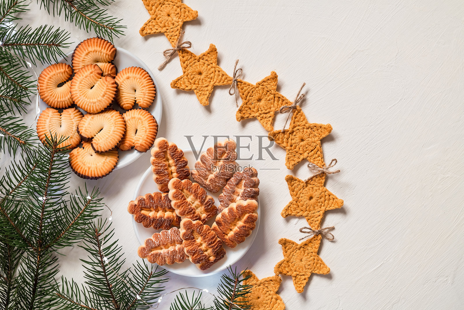 节日圣诞饼干摆放在盘子上，配有星星装饰和松树枝。黄油饼干在白色背景上。留白空间。照片摄影图片