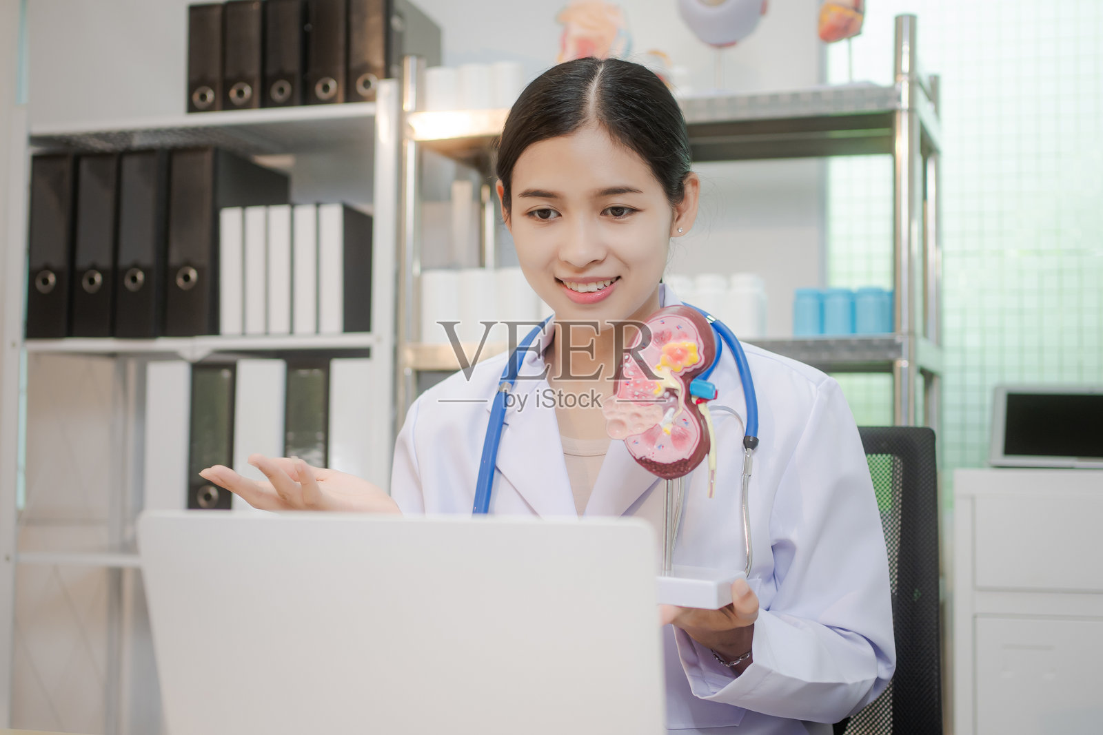 一位年轻的亚洲女性医生独自在桌前工作，审查与肾脏相关的医疗数据。在宁静的临床环境中，她专注于提供准确的诊断和治疗计划。照片摄影图片