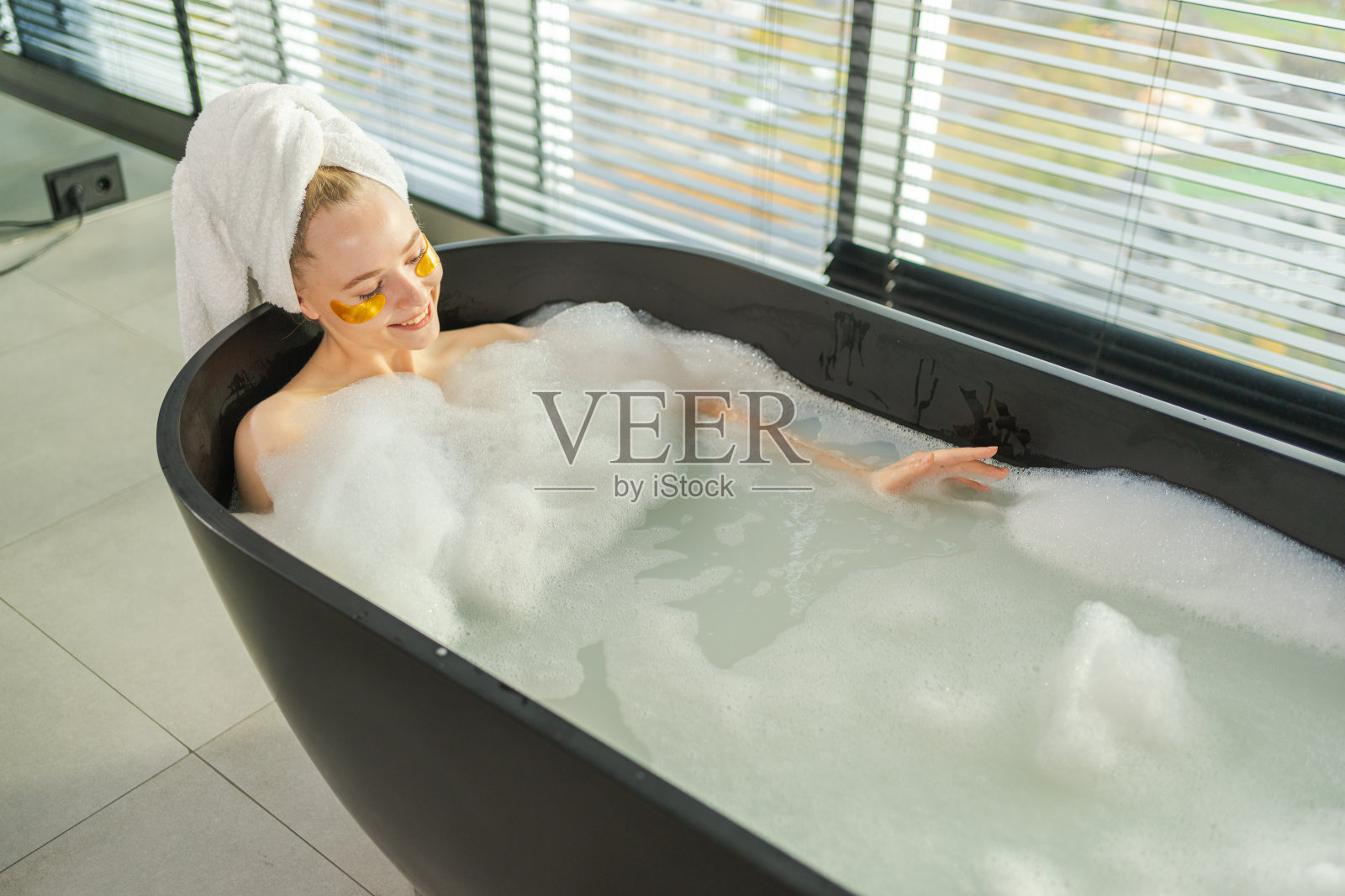 水疗放松。年轻女性躺在泡沫浴中。女孩在家中的浴室放松。漂亮的女性在浴室享受早晨的沐浴，美容护理身体肌肤的概念。照片摄影图片