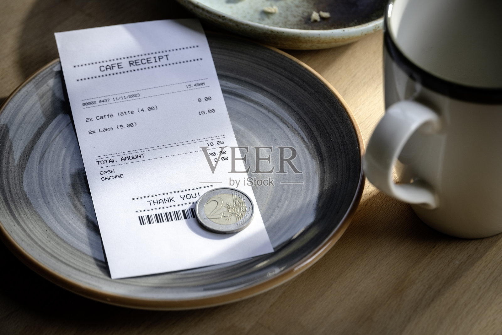 咖啡馆收据、欧元硬币和空咖啡杯放在桌子上照片摄影图片