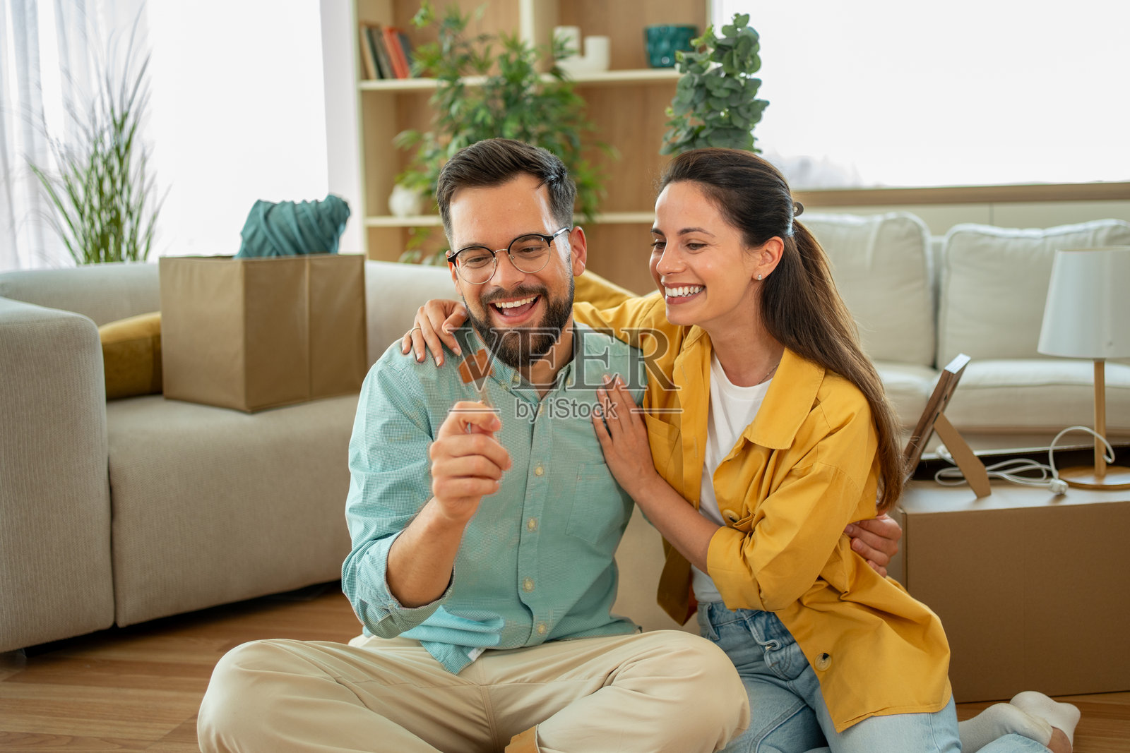 快乐的情侣坐在地板上，手握新房钥匙照片摄影图片