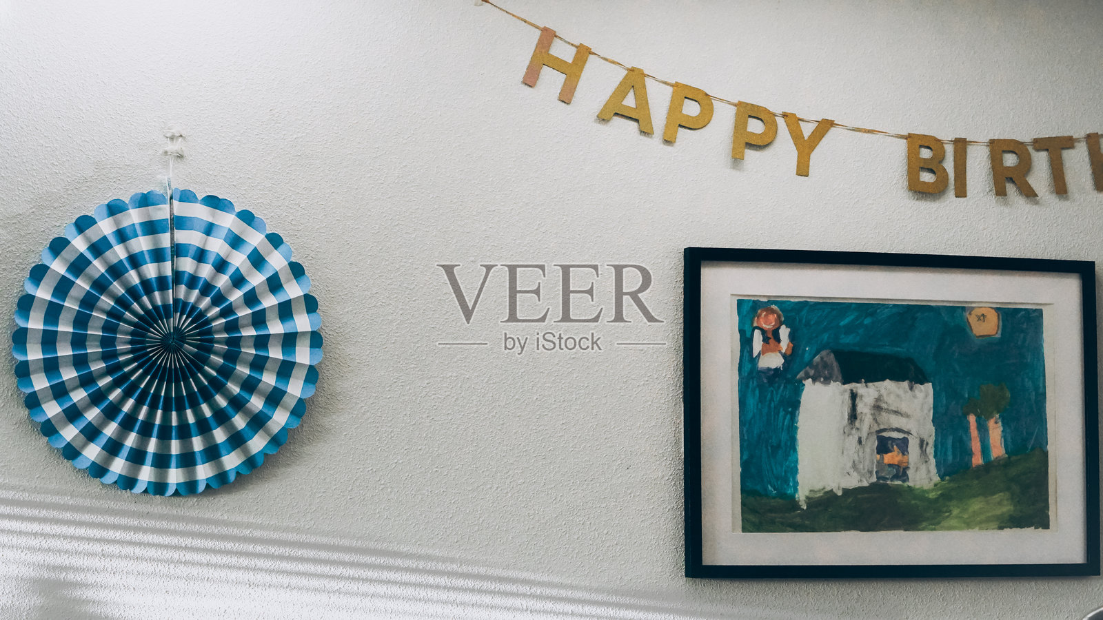 生日装饰墙，上面有金色的“生日快乐”横幅、条纹扇子装饰和孩子的房子画框作品照片摄影图片
