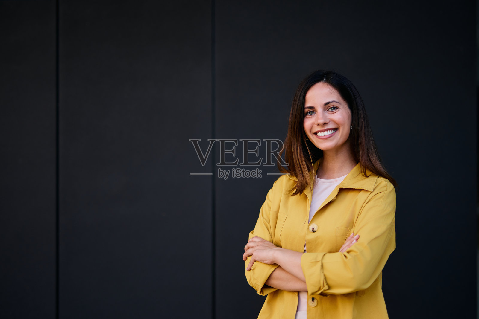 自信的女性穿着黄色夹克，微笑着站在深色背景前照片摄影图片