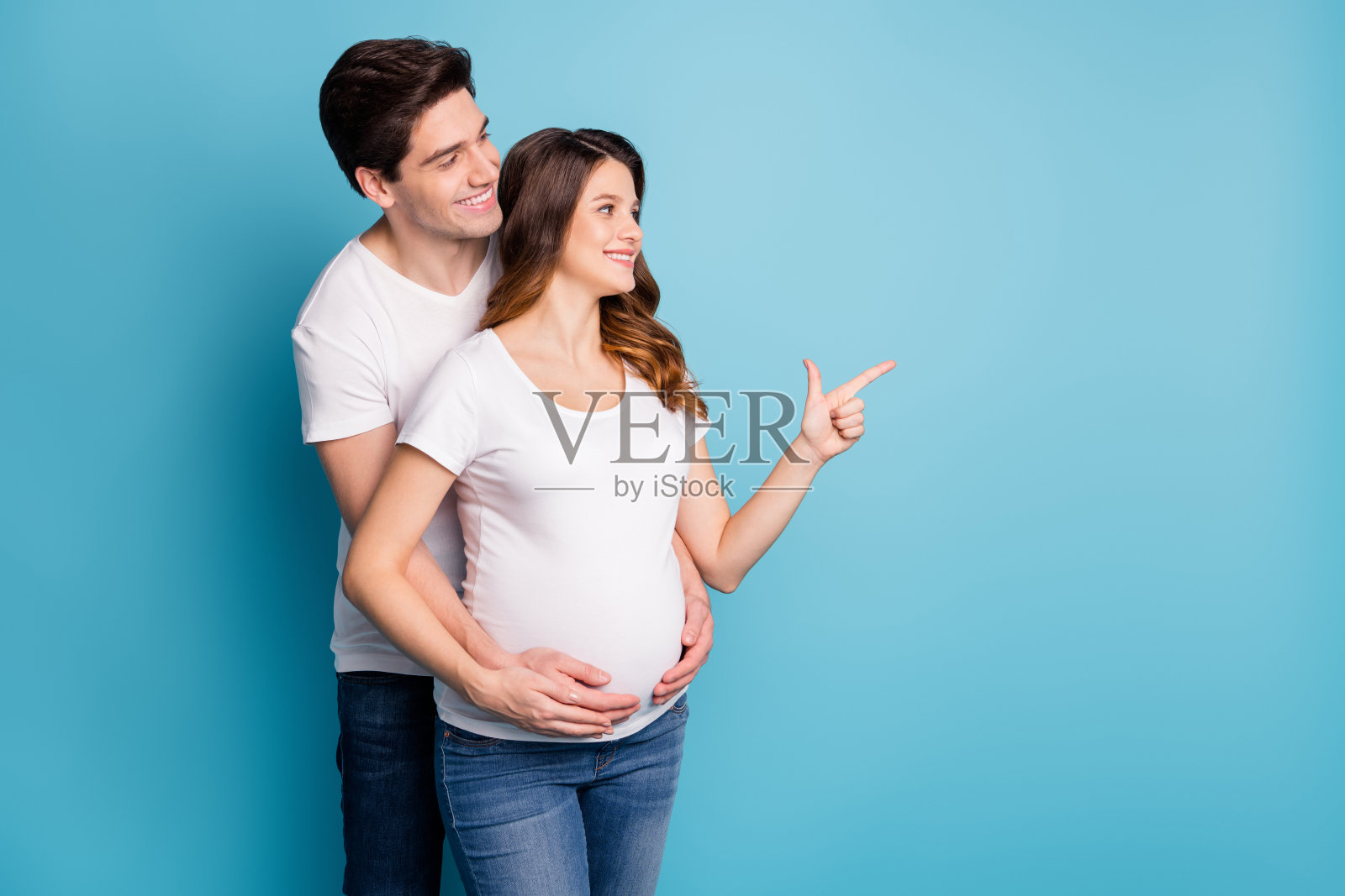 年轻快乐的情侣面带微笑，手指指向蓝色背景上的空白处。照片摄影图片