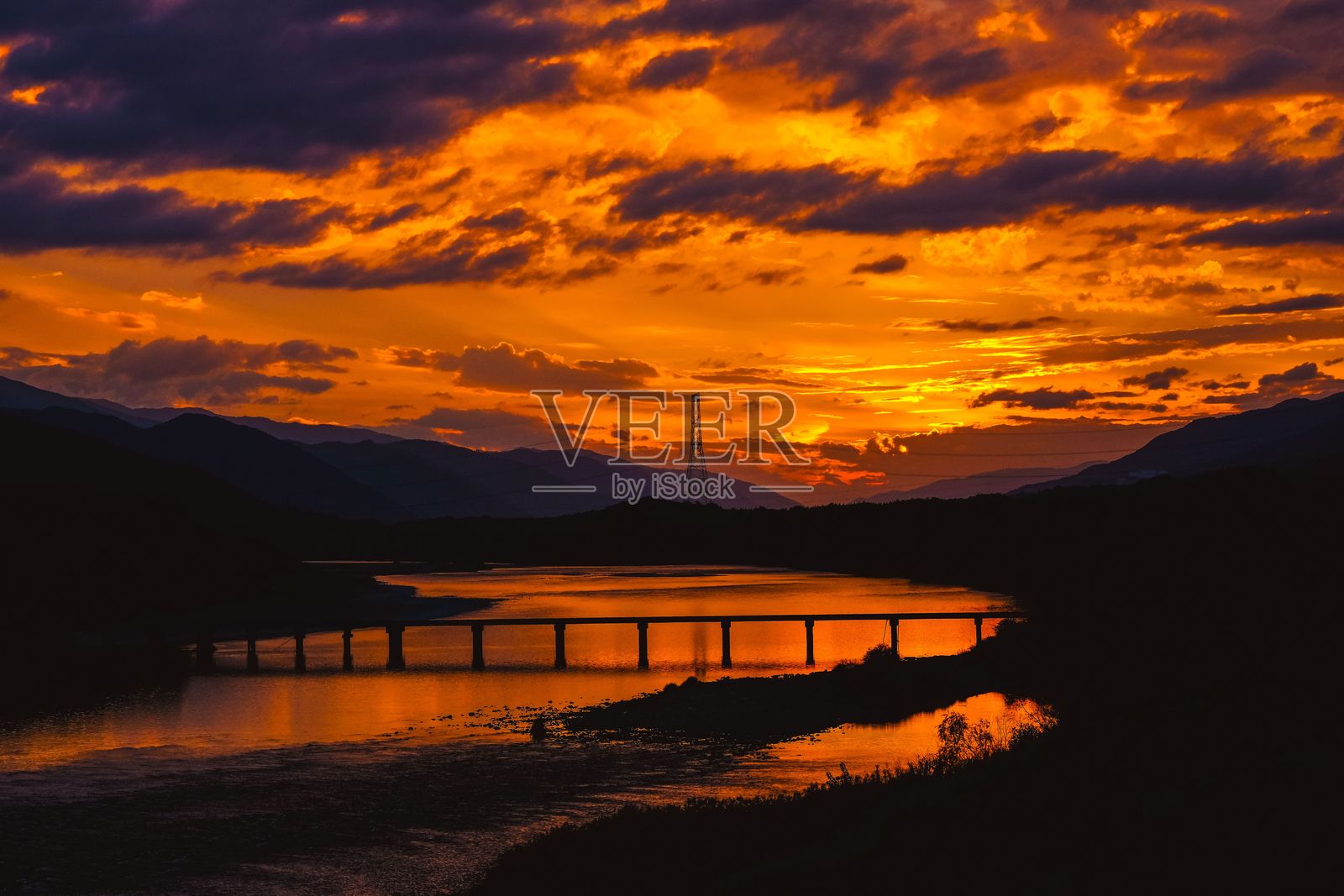 河流和桥梁剪影下的绚丽日落。照片摄影图片
